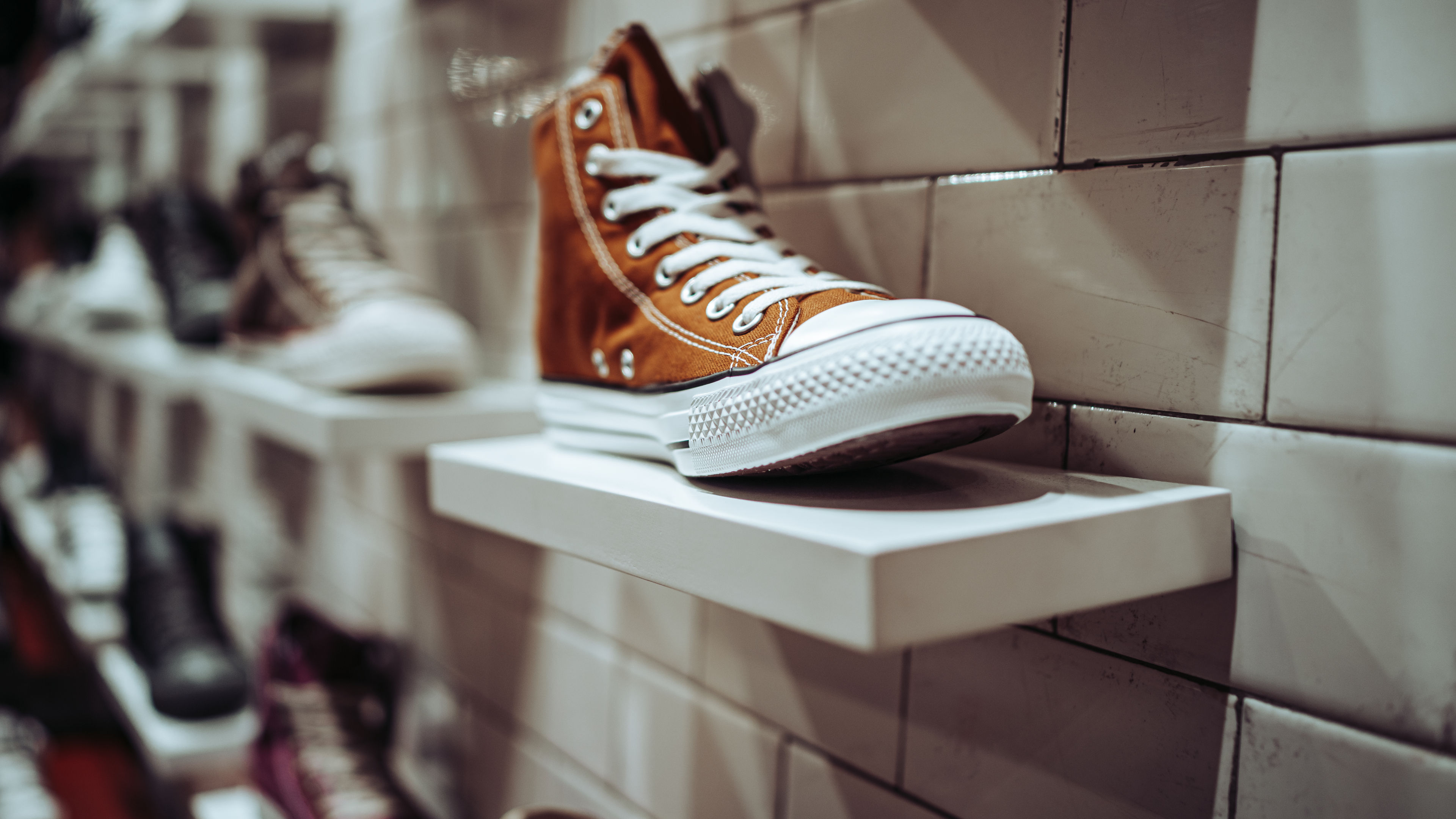 A brown high-top sneaker with white laces displayed on a shelf against a tiled wall in a shoe store.