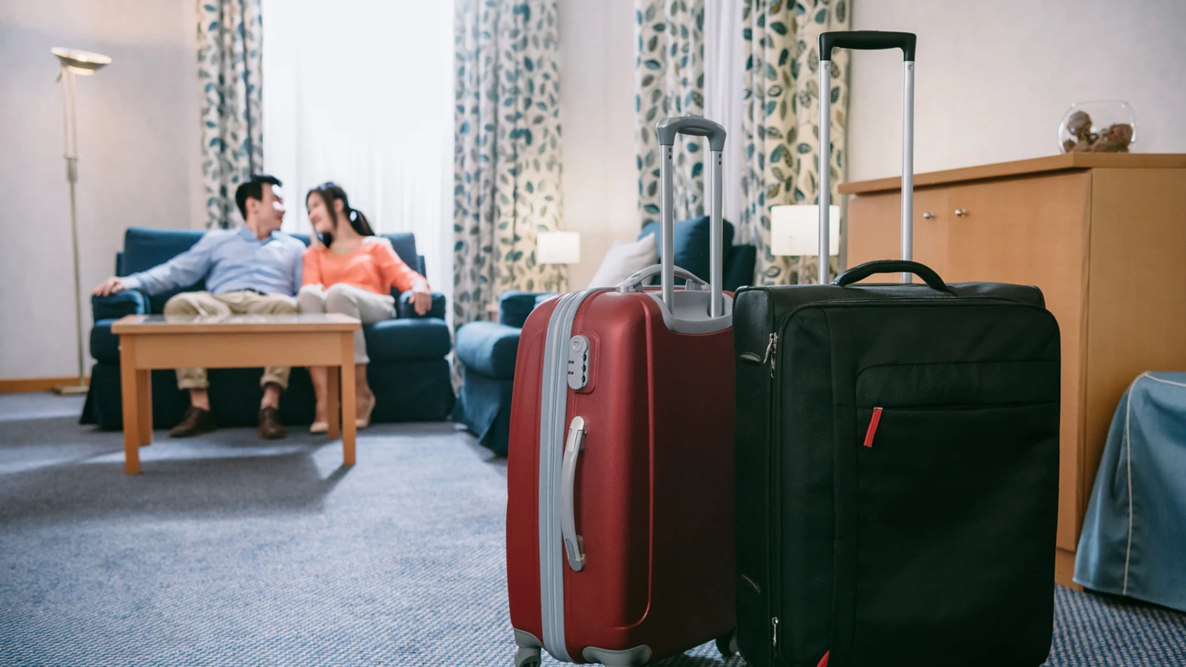 Close-up view of two suitcases and mature Asian couple sitting on sofa in hotel room.