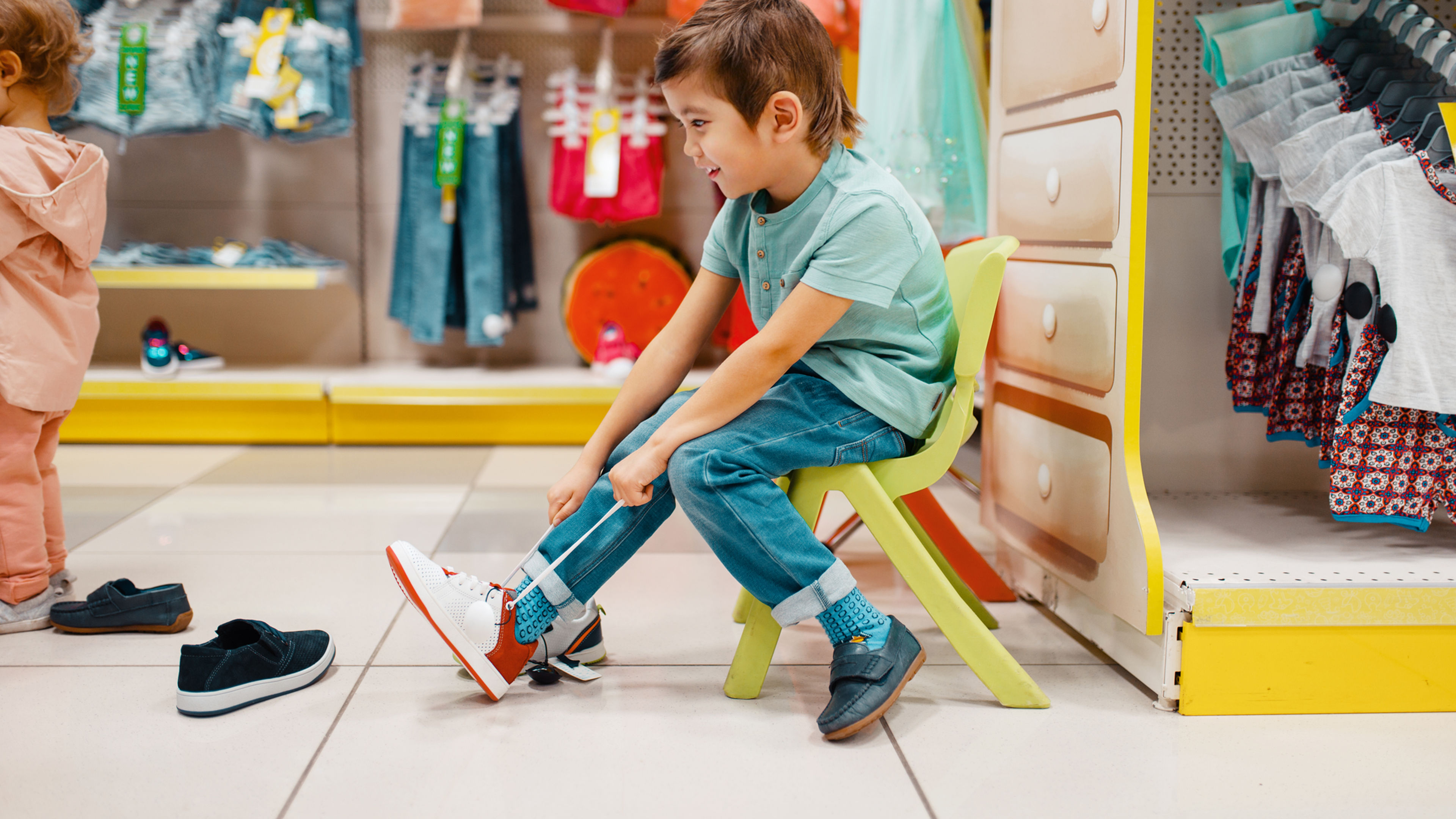 Little Asian boy trying on shoes in kids store.