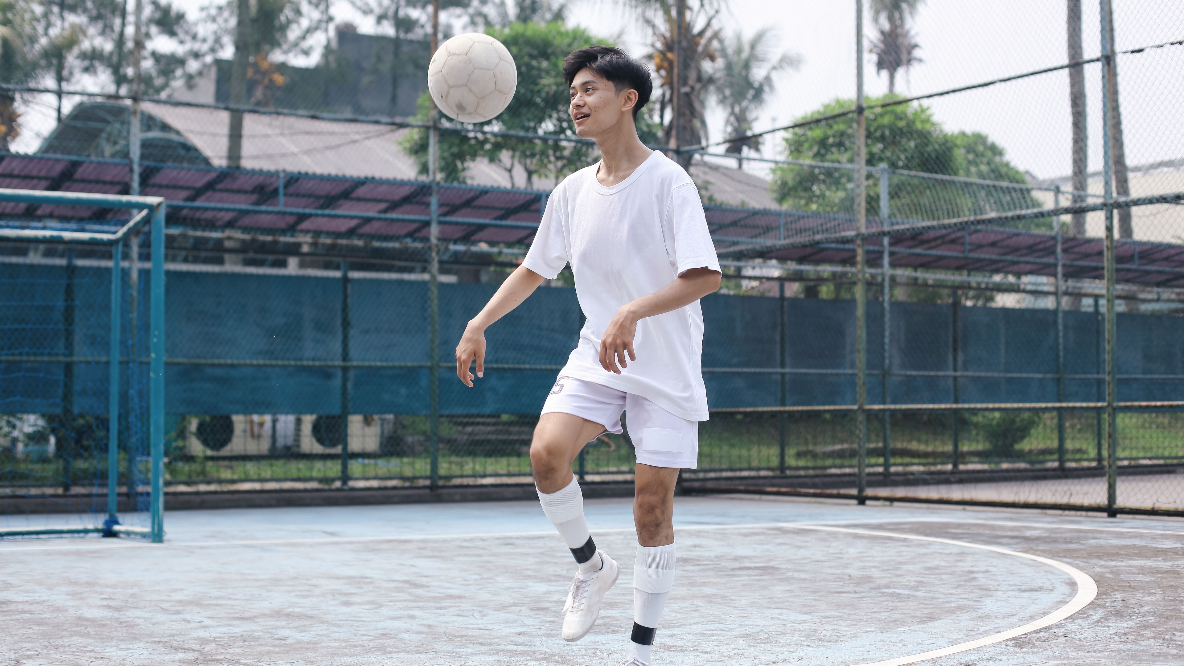 A young man in white juggling football in a turf.