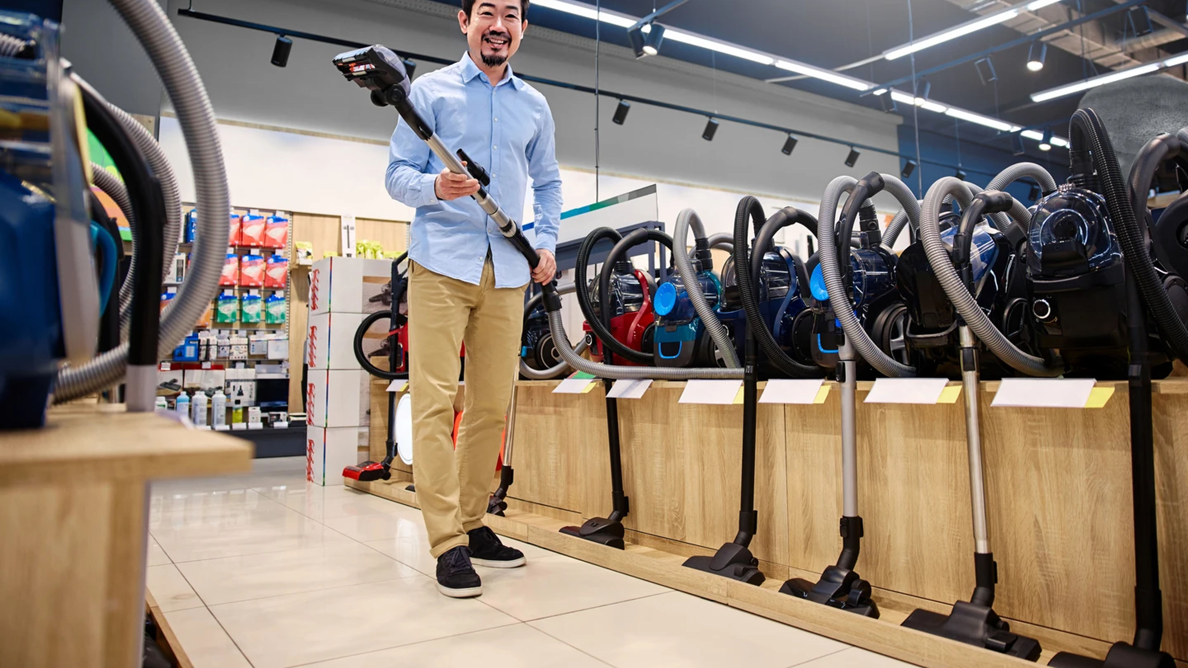 A young man actively explores a wide range of various vacuum cleaner options available in a contemporary appliance store