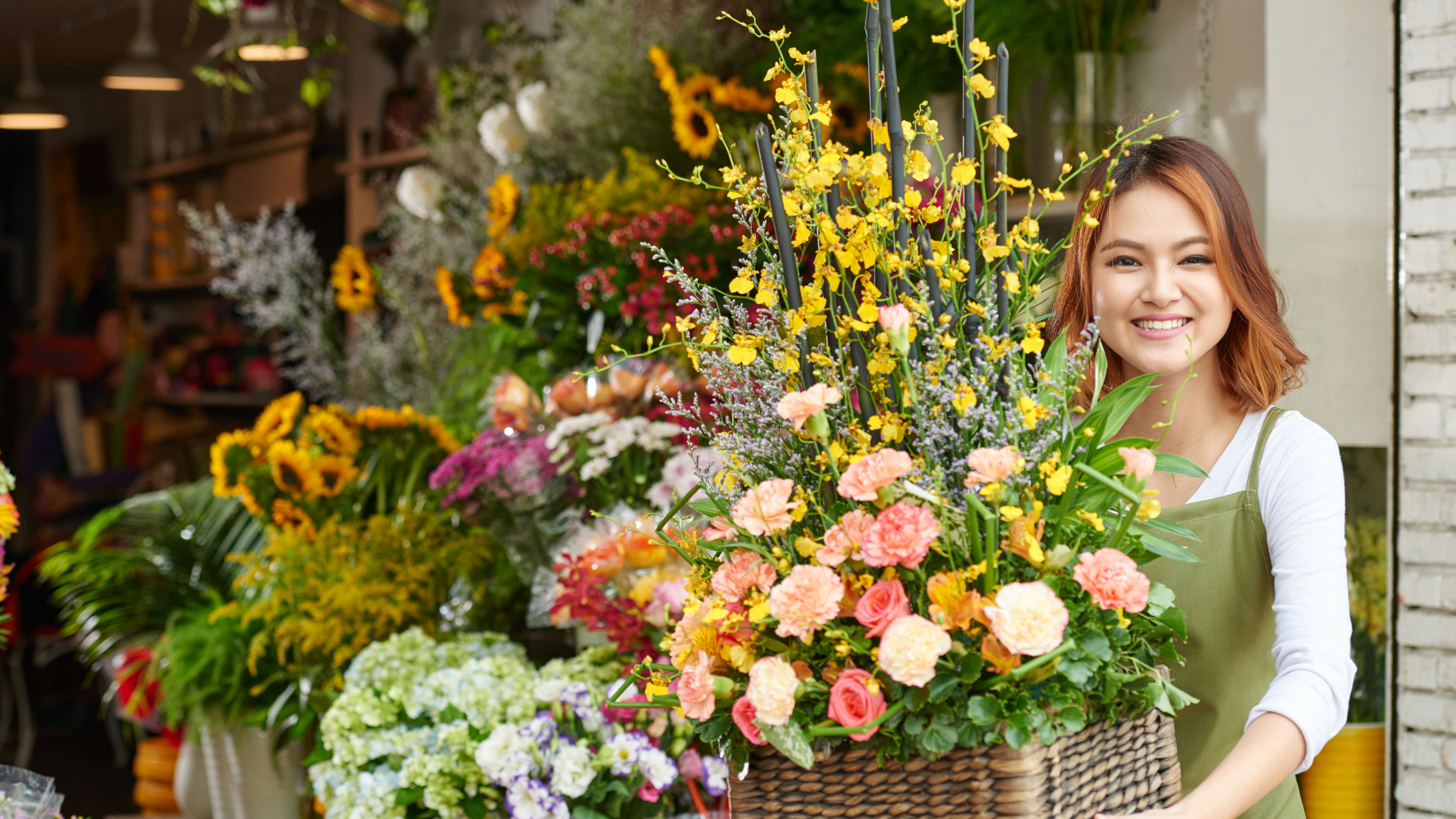 Pretty flower shop owner holding a bouquet, standing in front of a vibrant display of flowers.