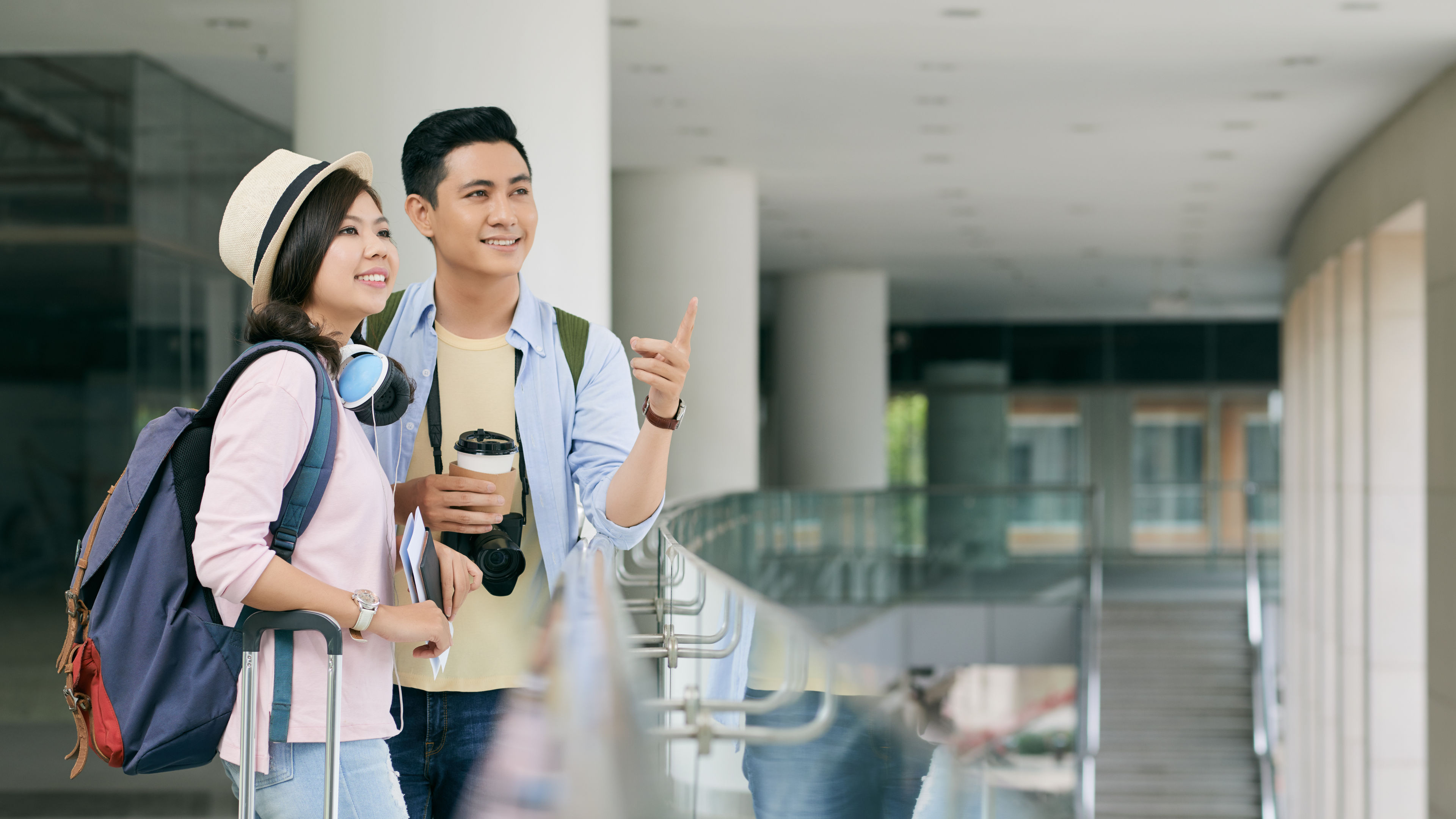 A young couple with luggage, backpacks, and coffee cups.