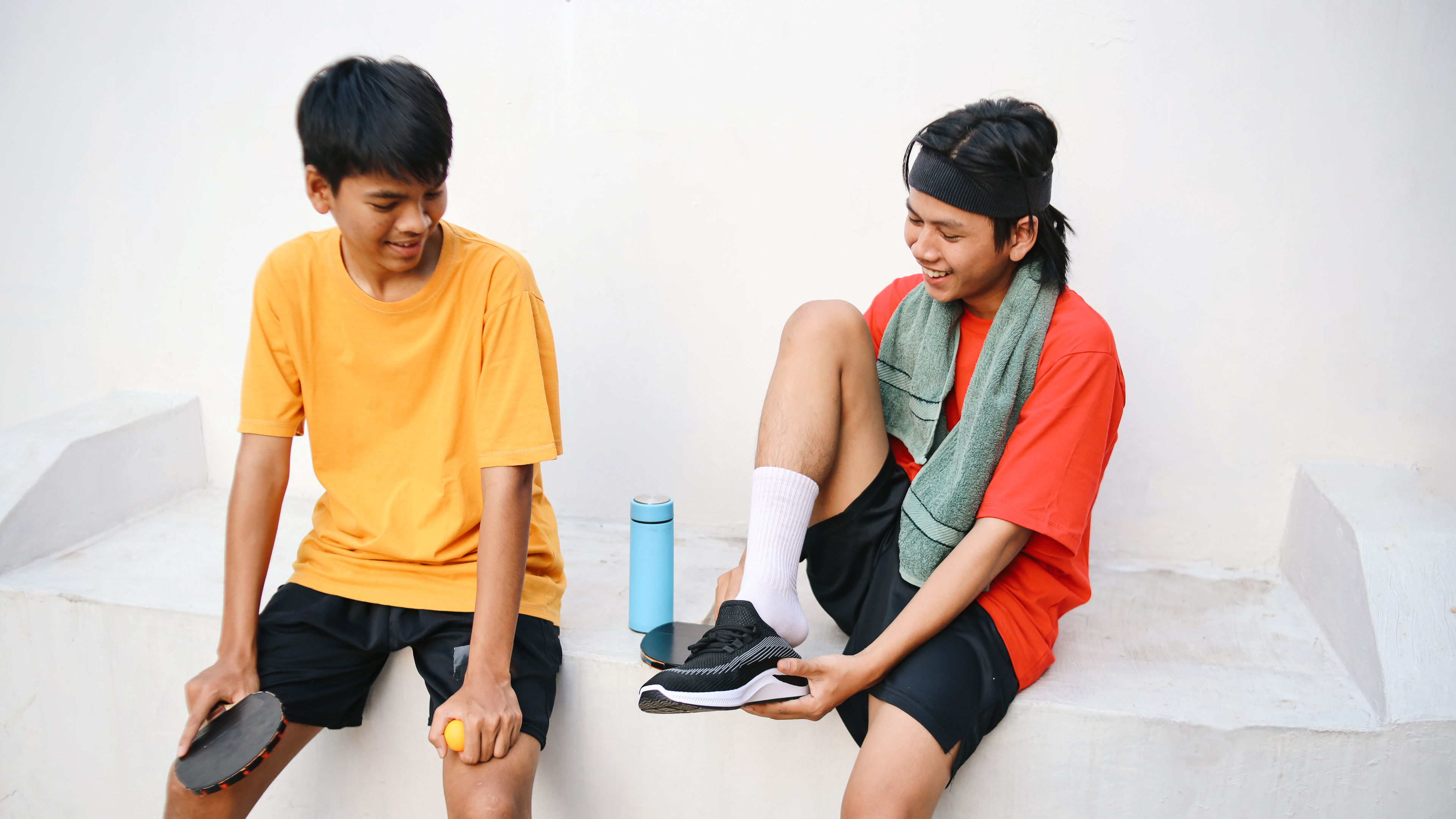 Two men are tying a pair of shoes