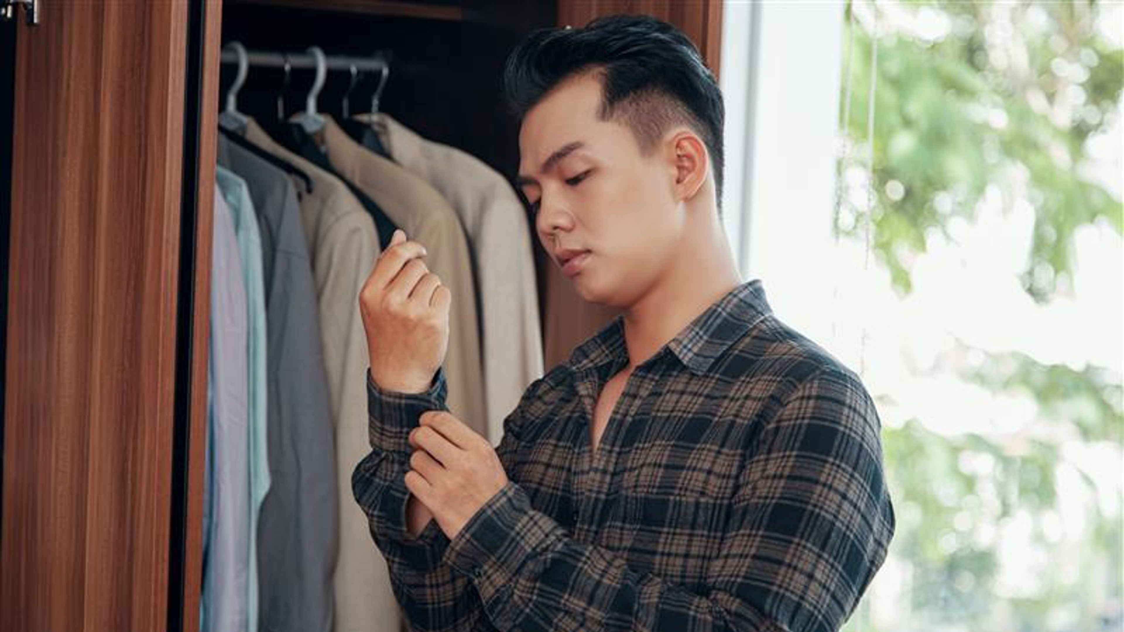 Young handsome Asian man buttoning shirt
